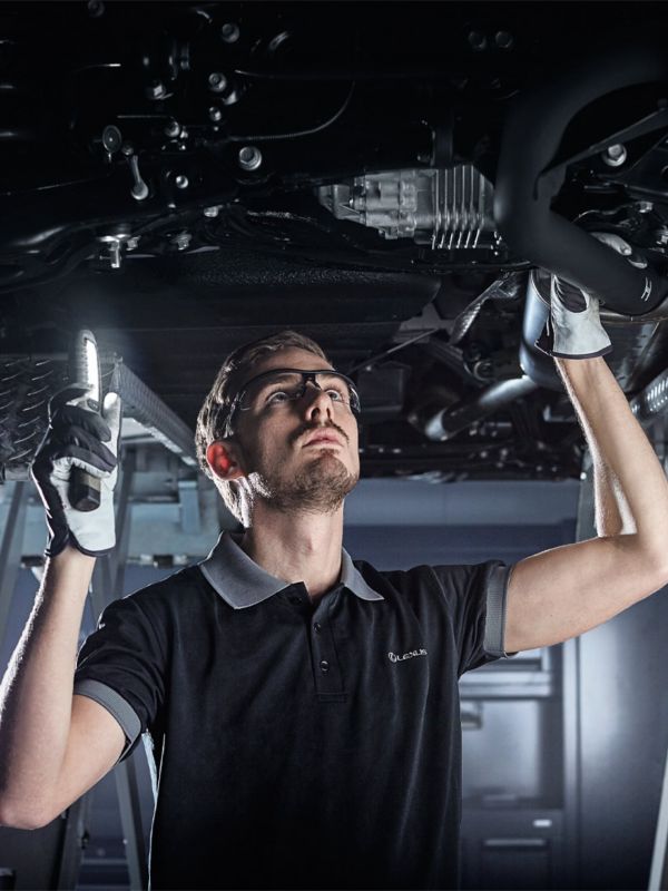 Ein Mechaniker steht unter einem Lexus auf einer Hebebühne und begutachtet das Fahrzeug