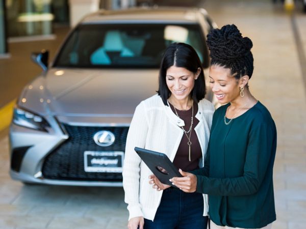 Zwei Personen stehen vor einem Lexus in einer Werkstatt und betrachten ein Tablet