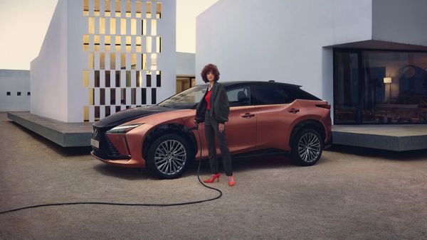 Eine Person steht vor einem vor einem Haus geparkten Lexus der mit einem Kabel zum Laden angeschlossen ist