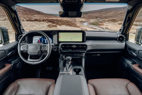 Innenansicht eines modernen Fahrzeugs mit Armaturenbrett, Lenkrad und großem Touchscreen-Display mit Navigationsfunktionen vor einer malerischen Kulisse.