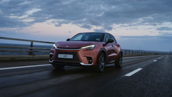Ein kupferfarbener Lexus LBX fährt vor einem bewölkten Himmel eine Straße entlang